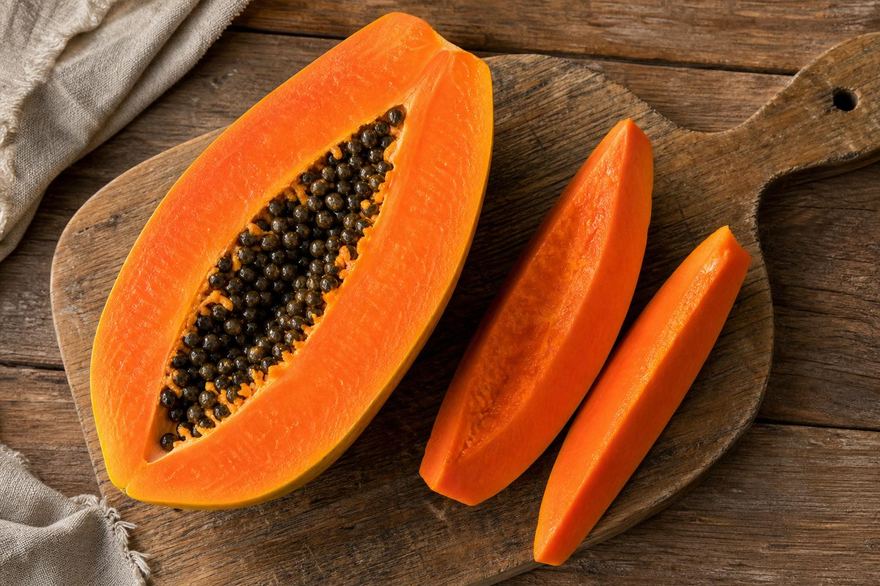Ripe papaya cut open on a wooden cutting board, showing orange flesh and black seeds